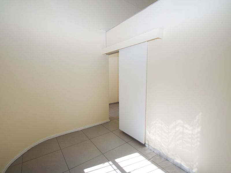 A bright, empty office space featuring neutral walls, tiled flooring, and a functional sliding door, offering a clean and versatile workspace.