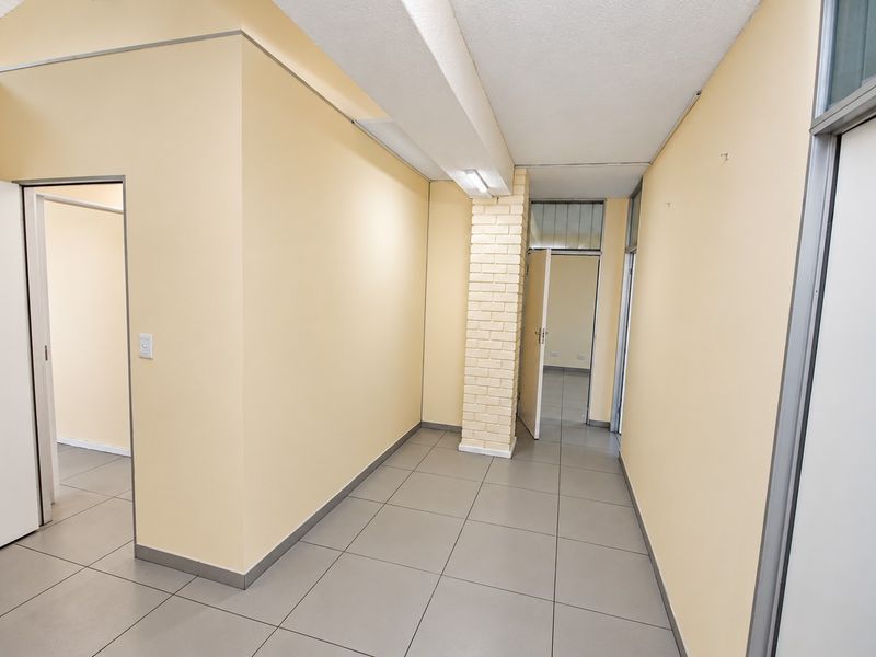 A vacant office space featuring neutral walls, tiled flooring, and a distinctive exposed brick column, offering a clean and functional layout.