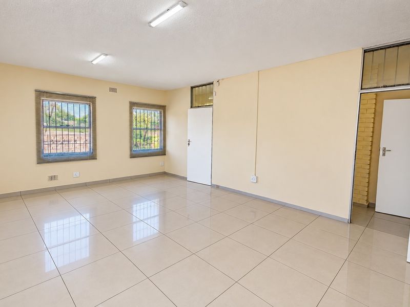 A spacious, empty office area featuring neutral tiled flooring, bright overhead lighting, and secure windows, offering a clean and versatile workspace.