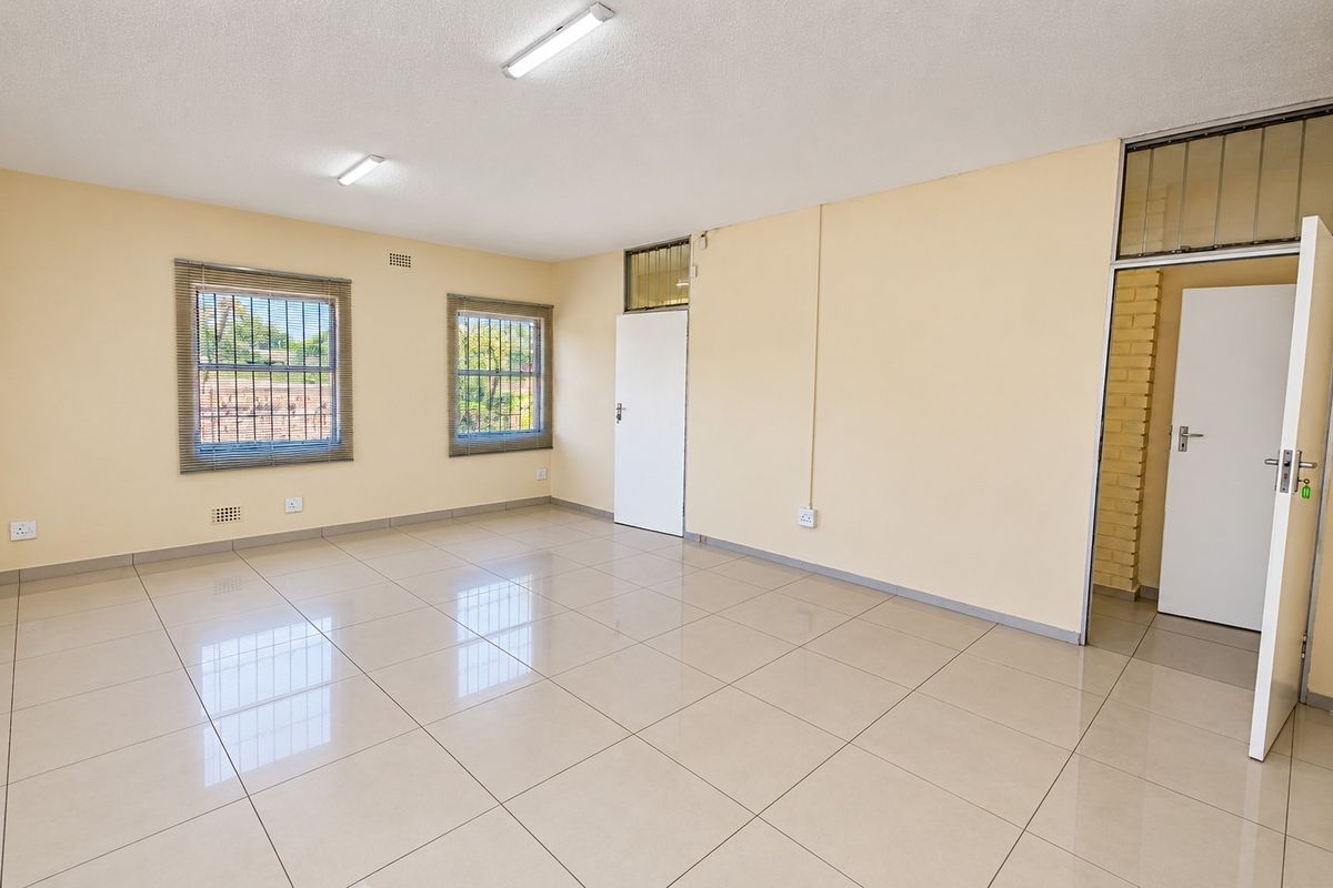 A spacious, empty office area featuring neutral tiled flooring, bright overhead lighting, and secure windows, offering a clean and versatile workspace.