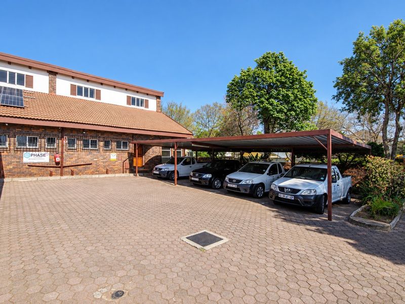 Exterior view of the office building featuring a brick facade, tiled roof with solar panels, and a paved parking area with a covered carport.