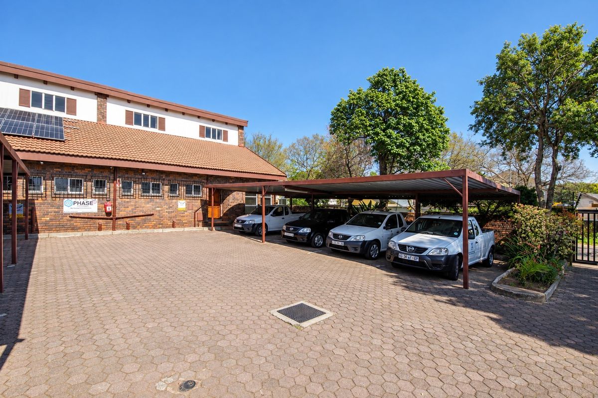 Exterior view of the office building featuring a brick facade, tiled roof with solar panels, and a paved parking area with a covered carport.