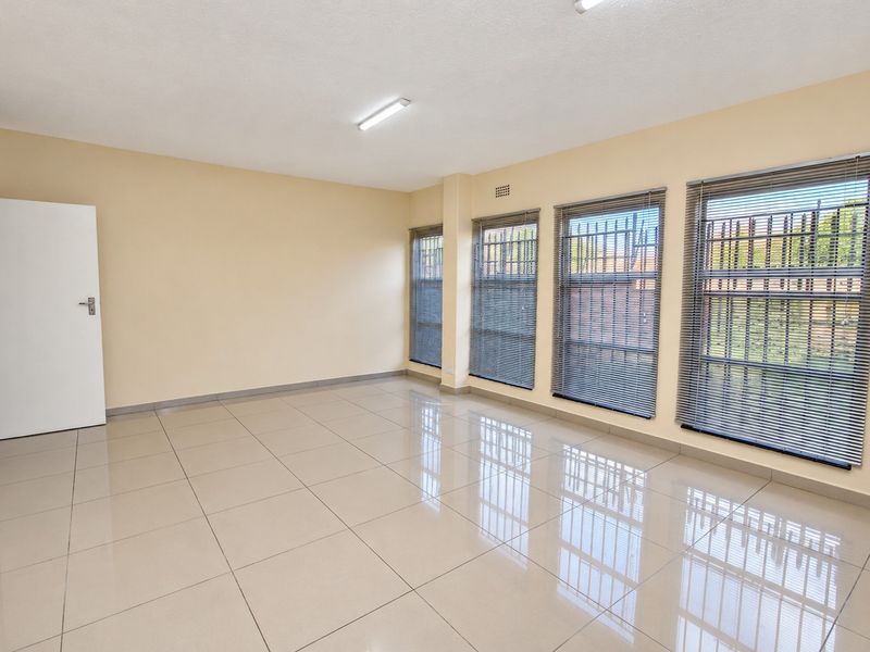 A bright, vacant office space featuring polished porcelain floor tiles, large windows with security bars, and neutral wall finishes.