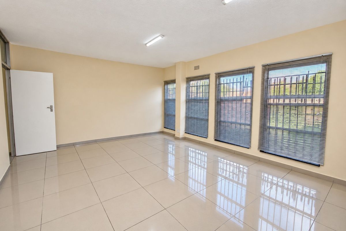 A bright, vacant office space featuring polished porcelain floor tiles, large windows with security bars, and neutral wall finishes.