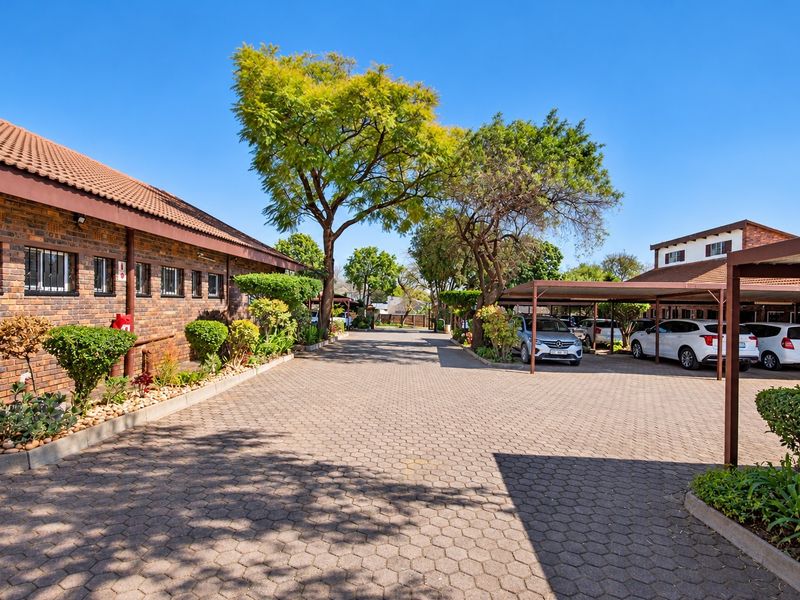 Exterior view of an office complex featuring a brick facade, paved driveway, and covered parking bays with established landscaping.