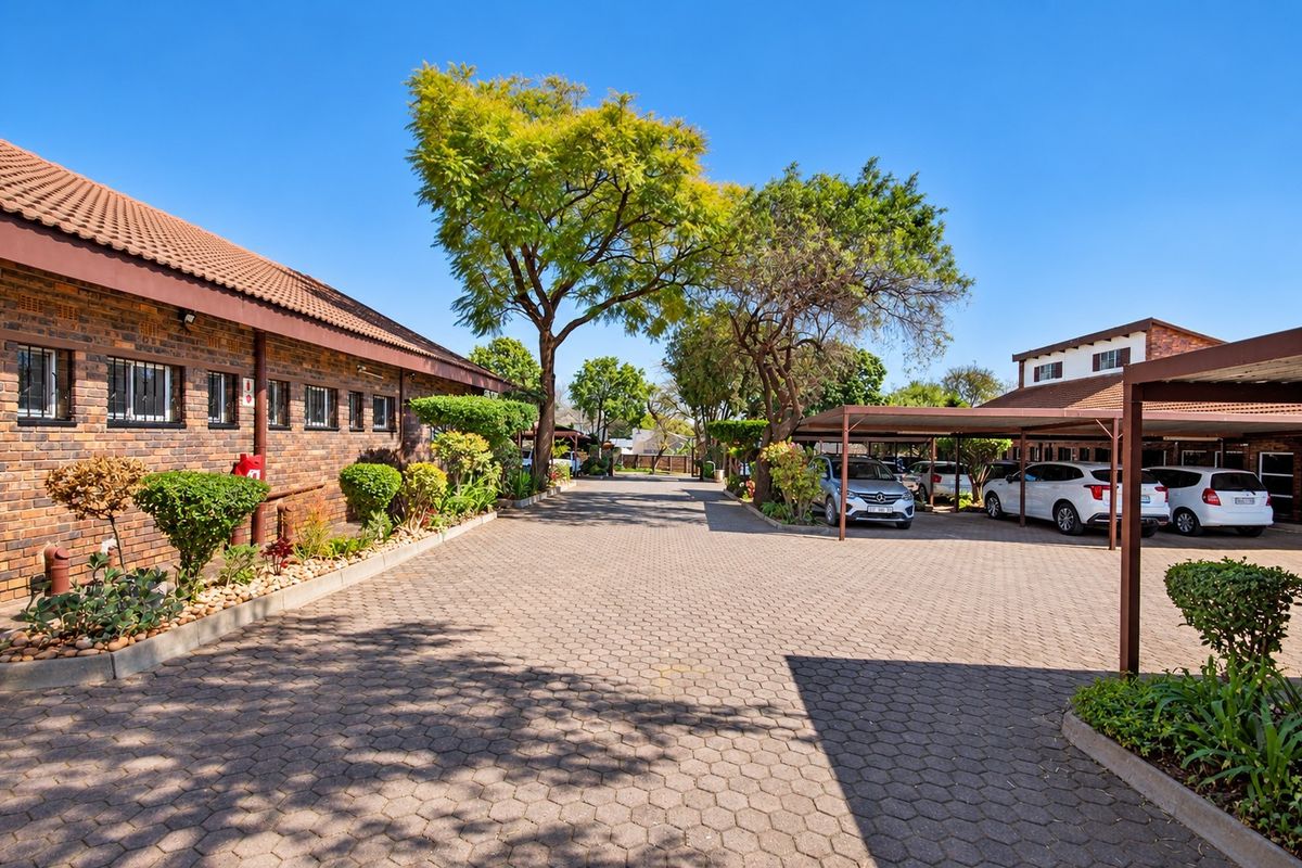 Exterior view of an office complex featuring a brick facade, paved driveway, and covered parking bays with established landscaping.
