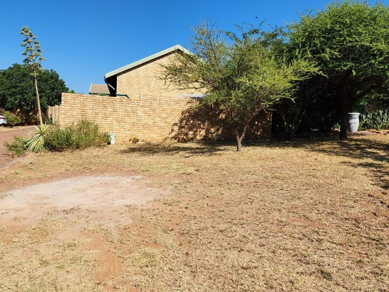 A view of the vacant residential land featuring a brick boundary wall, established trees, and access to the paved driveway.