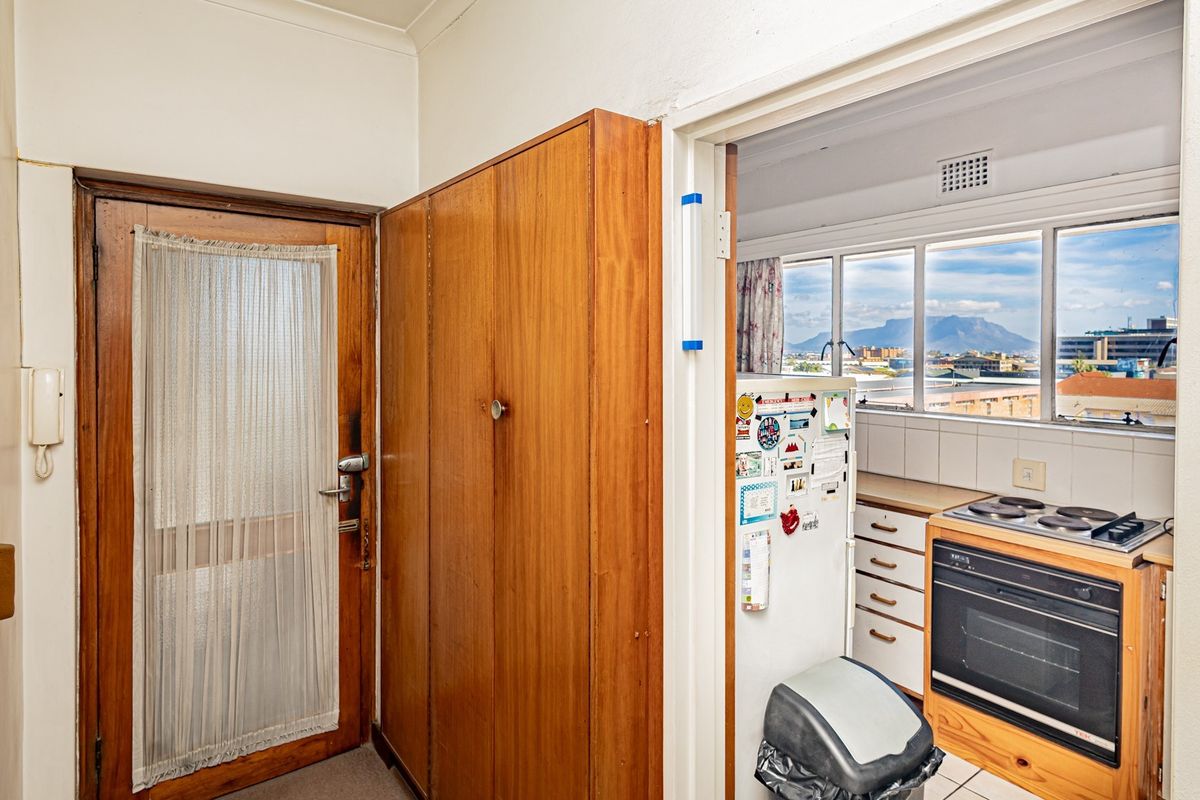 A compact kitchen featuring built-in cabinetry, an electric oven and hob, with a view of the city and mountain through the window.