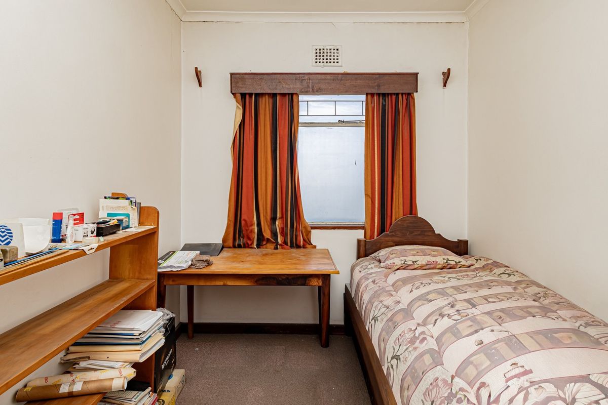 A compact bedroom featuring a single window with a wooden pelmet and a ventilation grille, offering a functional space for a single bed.