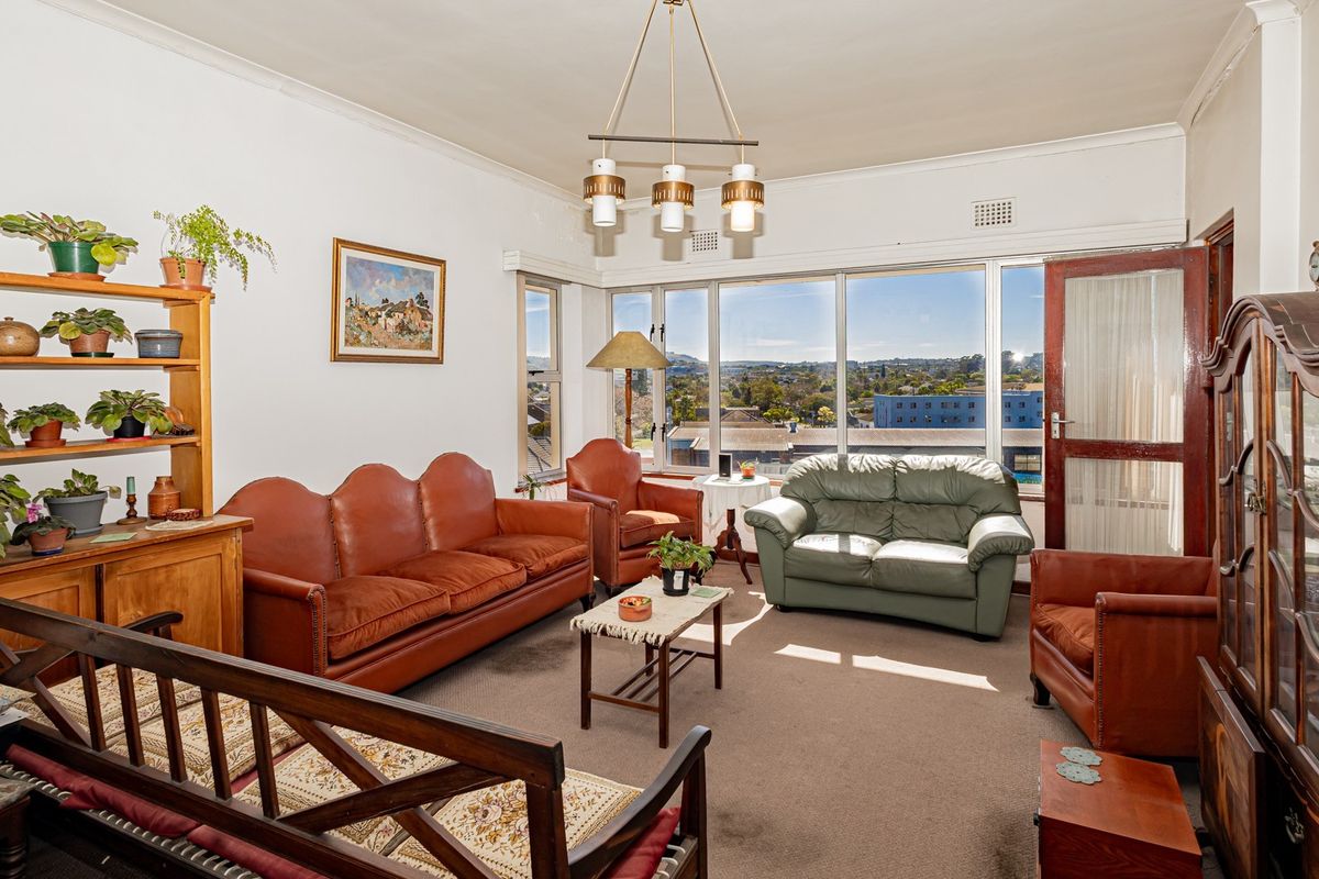 A spacious living room featuring large windows with expansive city views, neutral walls, and carpeted flooring, offering a bright and comfortable living space.