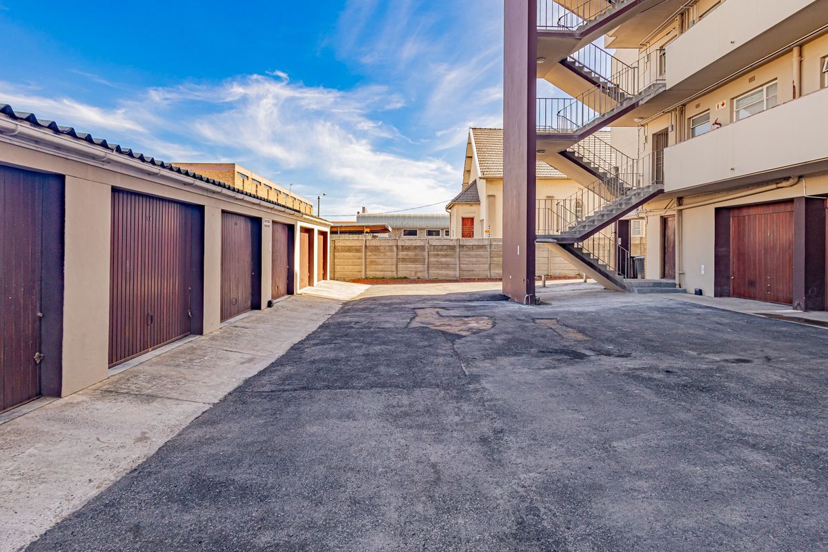 Rear exterior view of the apartment complex featuring a row of garages, an external staircase, and a paved driveway area.