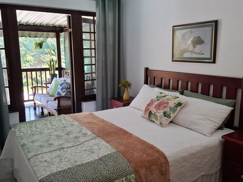 A well-maintained bedroom featuring timber-framed glass doors that open onto a private covered balcony with a timber balustrade.