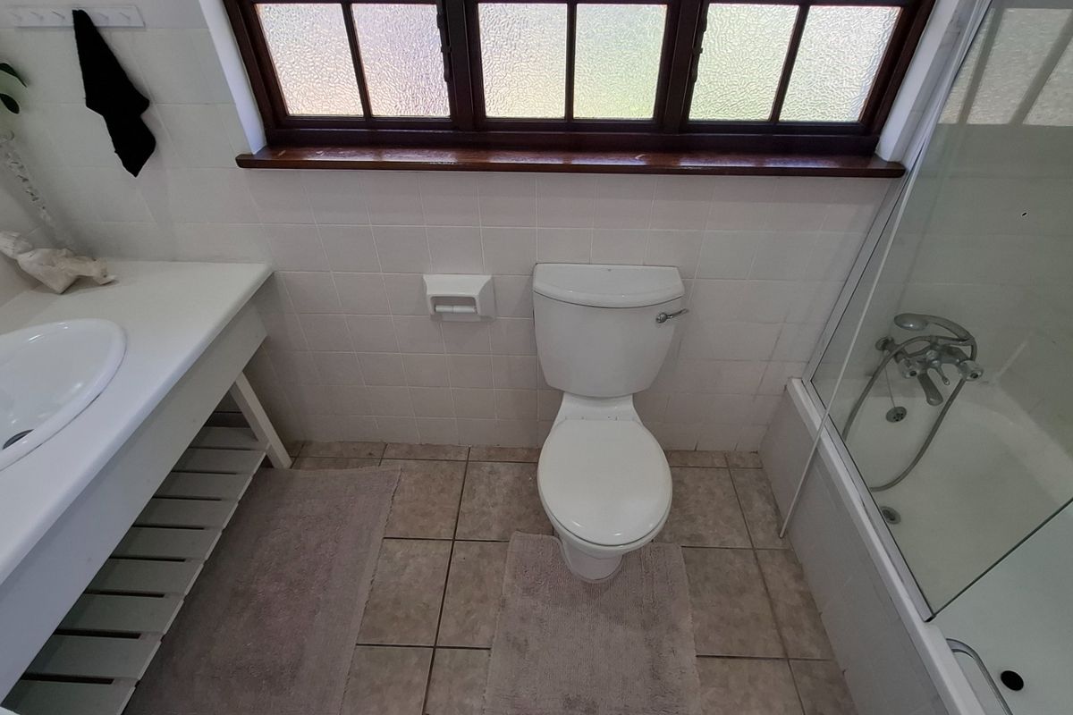 A functional bathroom featuring a built-in vanity, toilet, and a shower-over-bath combination with tiled finishes and a timber-framed window.