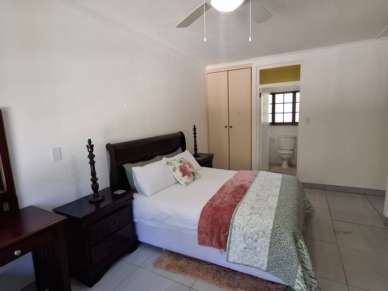 A bedroom featuring tiled flooring, a ceiling fan, and built-in cupboards, with direct access to an en-suite bathroom.