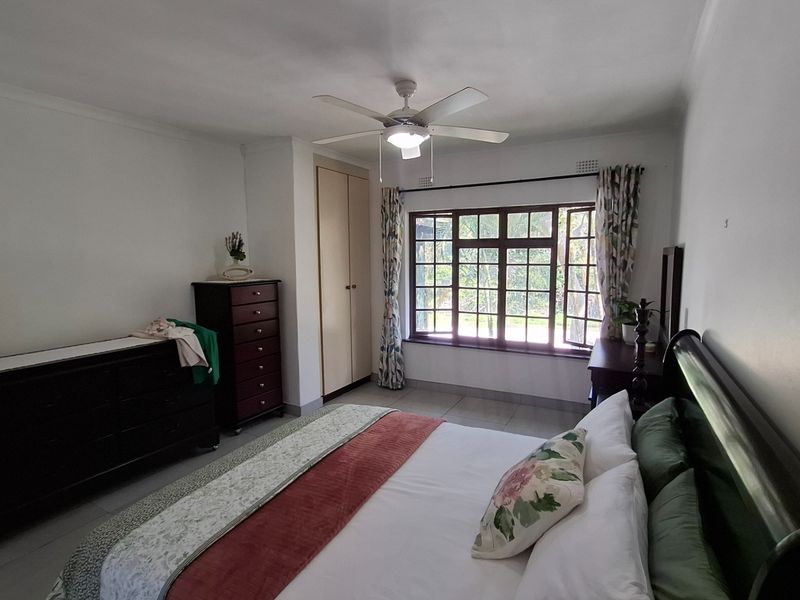 A well-lit bedroom featuring tiled flooring, a ceiling fan, and a built-in wardrobe, offering a comfortable and functional living space.