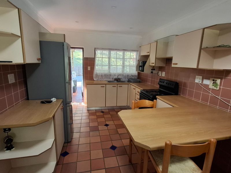 A functional kitchen featuring dated cabinetry, laminate countertops, a double basin sink, and ceramic tile flooring with direct access to the exterior.