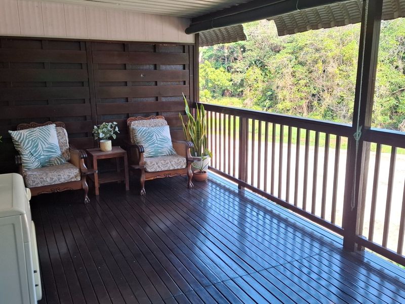 A covered timber balcony featuring dark wood decking and balustrades, offering an elevated outdoor space with a natural outlook.