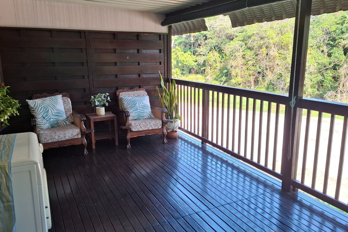 A covered timber balcony featuring dark wood decking and balustrades, offering an elevated outdoor space with a natural outlook.