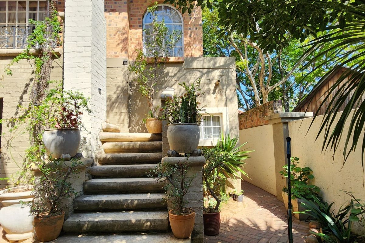 A rear exterior view featuring a brick staircase leading to an upper level, complemented by brick paving and established garden elements.
