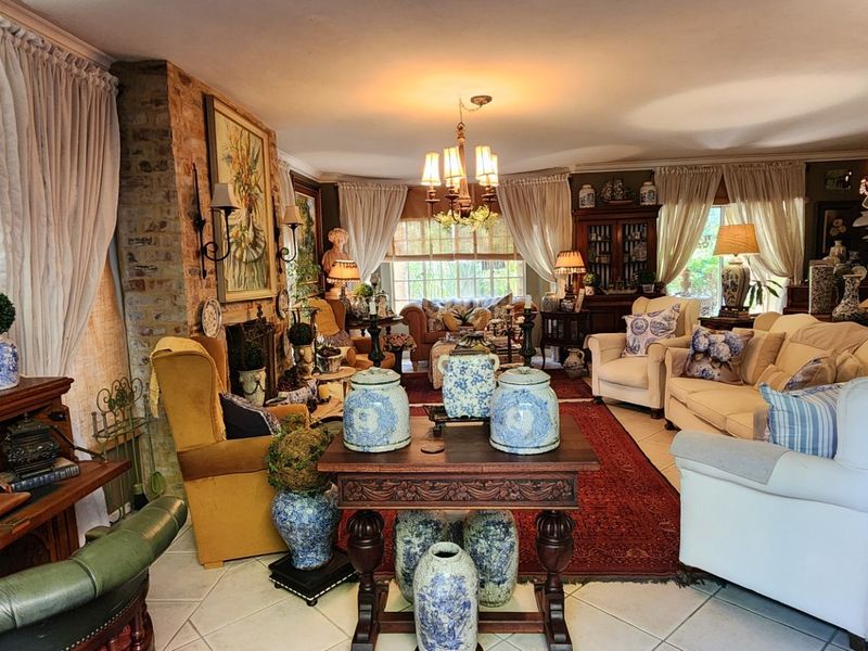A spacious living room featuring an exposed brick fireplace, tiled flooring, and classic chandelier lighting, creating a warm and traditional atmosphere.