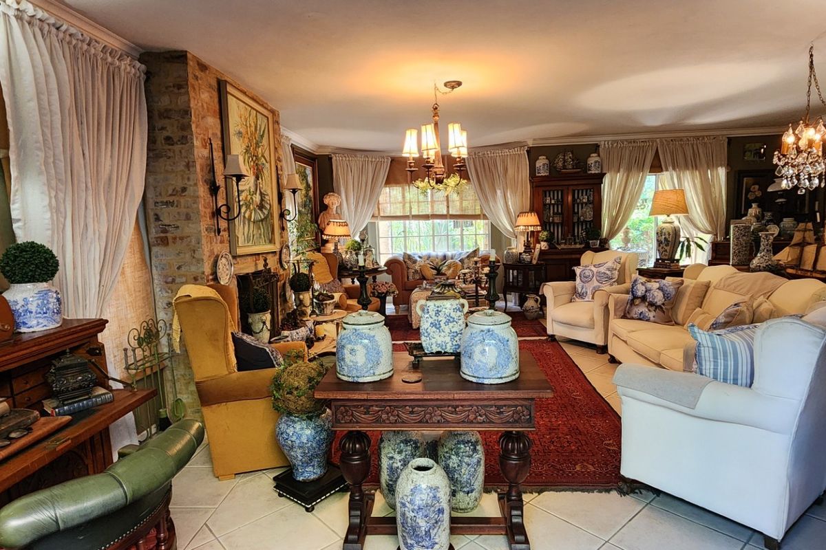 A spacious living room featuring an exposed brick fireplace, tiled flooring, and classic chandelier lighting, creating a warm and traditional atmosphere.