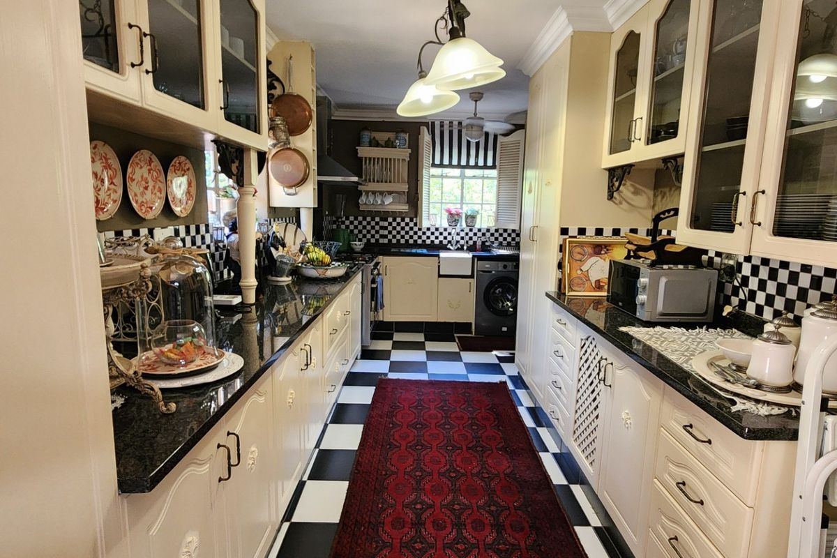 A galley-style kitchen featuring classic checkerboard flooring, cream cabinetry, granite countertops, and an apron-front sink with integrated laundry facilities.