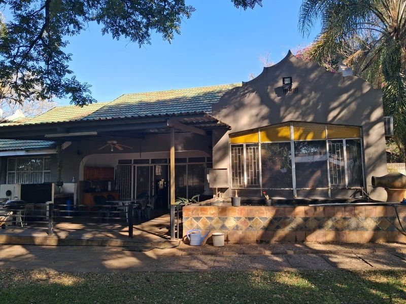 Rear view of the property featuring a covered patio area, stone-clad planter box, and traditional architectural detailing with security bars on windows.