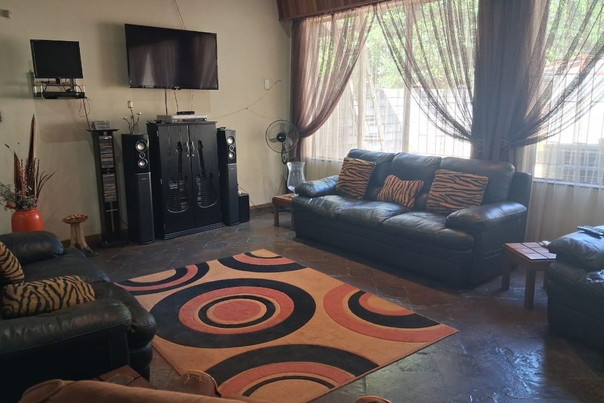 A spacious living room featuring natural stone tile flooring and a large window with a wooden pelmet, offering a comfortable and functional living space.