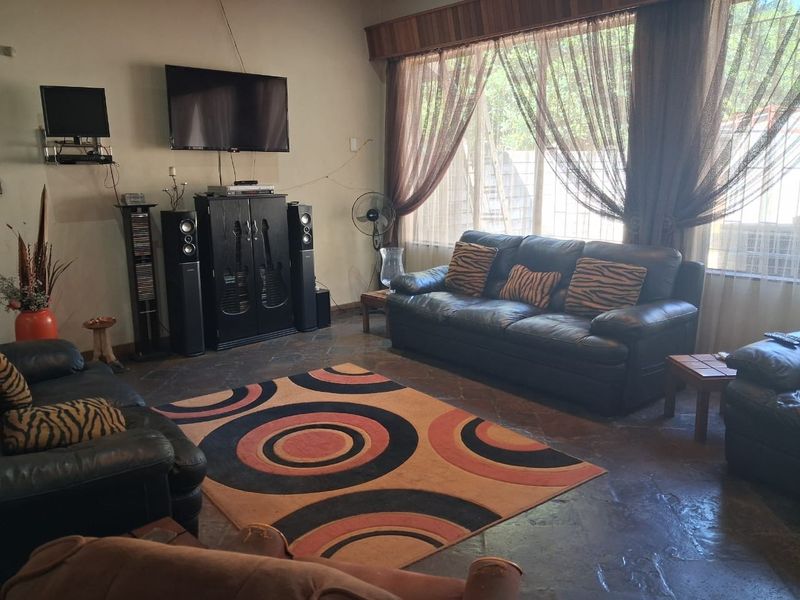 A spacious living room featuring natural stone tile flooring and a large window with a wooden pelmet, offering a comfortable and functional living space.