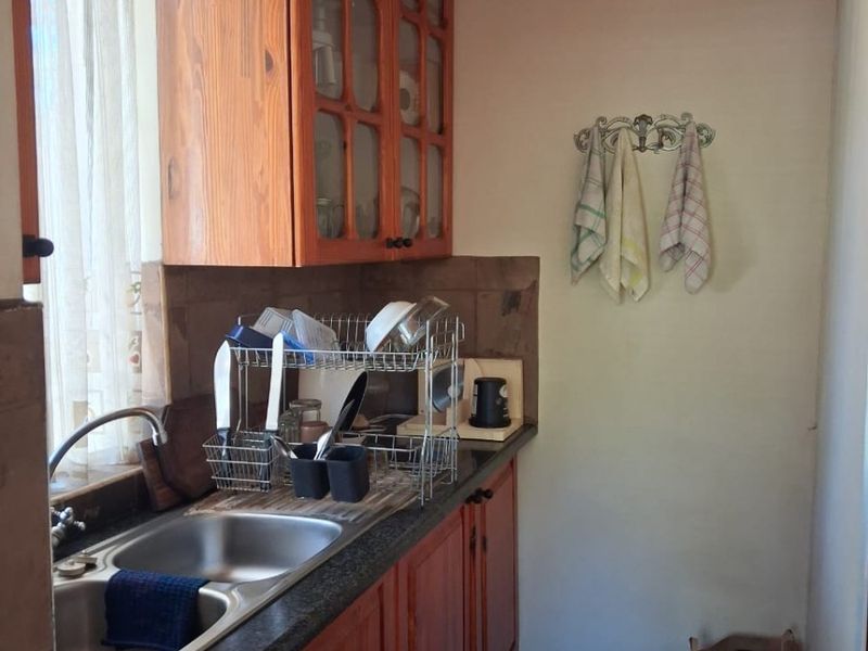 A functional scullery area featuring wooden cabinetry, stone countertops, and a double stainless steel sink with a tiled backsplash.
