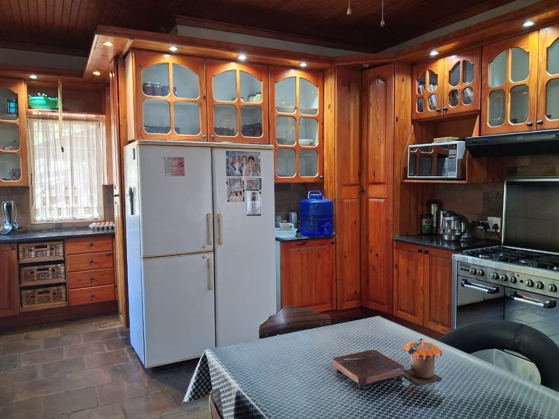 Spacious kitchen featuring extensive solid wood cabinetry, built-in appliances, stone tile flooring, and a warm timber ceiling, offering a traditional aesthetic.