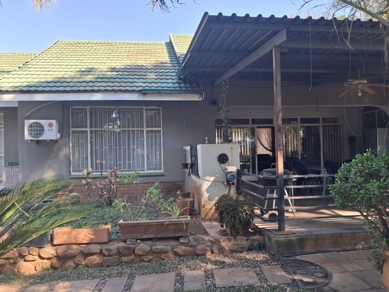 Rear view of the property featuring a covered patio, built-in braai, and established garden area with stone retaining wall.