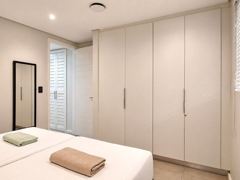 A well-maintained bedroom featuring neutral tones, ample built-in cupboard storage, recessed lighting, and tiled flooring with modern venetian blinds.