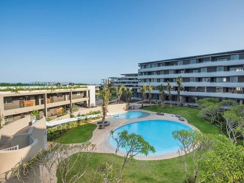 Aerial view of a modern apartment complex featuring a well-maintained swimming pool, water slide, and landscaped garden areas for resident recreation.