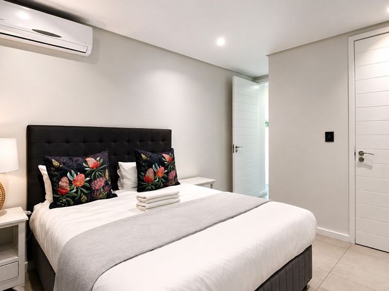 A well-maintained bedroom featuring tiled flooring, recessed downlighting, and a wall-mounted split-system air conditioning unit.