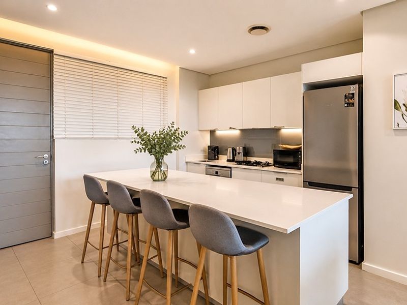 Modern kitchen featuring a central island with quartz countertops, sleek white cabinetry, integrated appliances, and recessed lighting, creating a clean and functional culinary space.