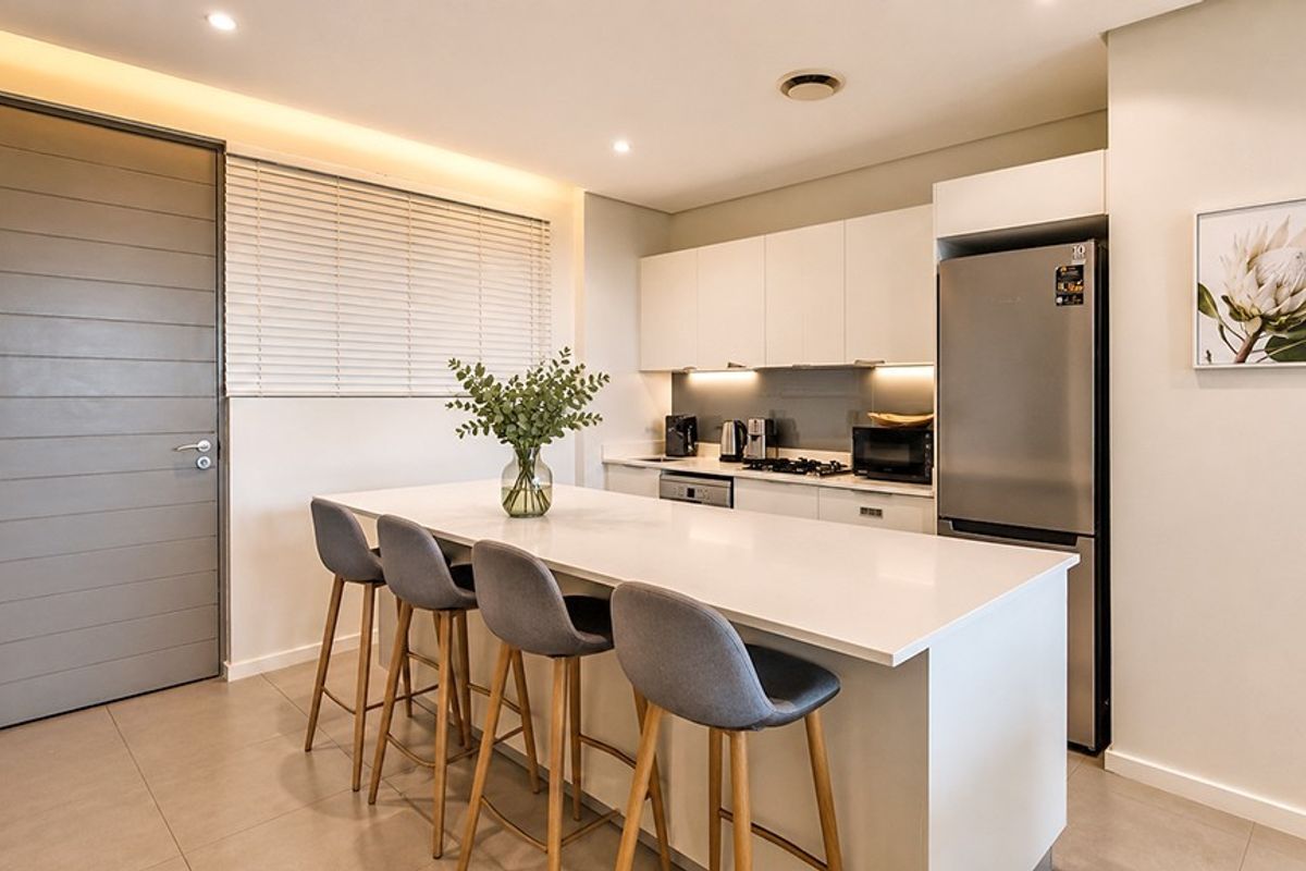 Modern kitchen featuring a central island with quartz countertops, sleek white cabinetry, integrated appliances, and recessed lighting, creating a clean and functional culinary space.