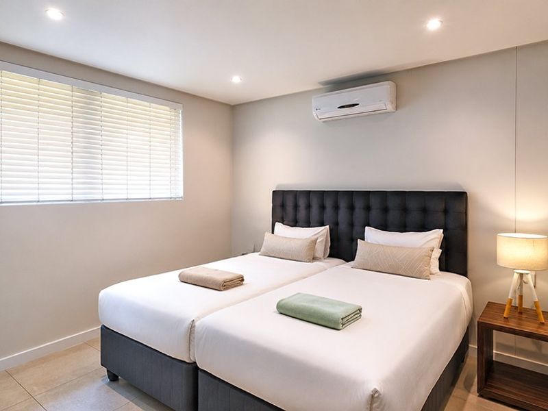 A well-maintained bedroom featuring tiled flooring, recessed downlighting, a wall-mounted split-system air conditioner, and venetian blinds.