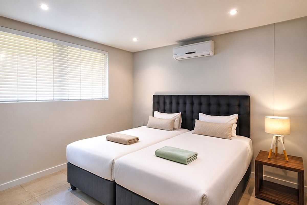 A well-maintained bedroom featuring tiled flooring, recessed downlighting, a wall-mounted split-system air conditioner, and venetian blinds.