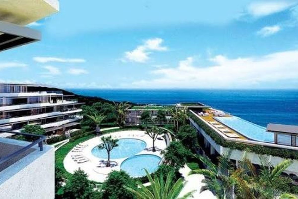 Aerial view of a modern apartment complex featuring swimming pools, landscaped gardens, and expansive ocean views.