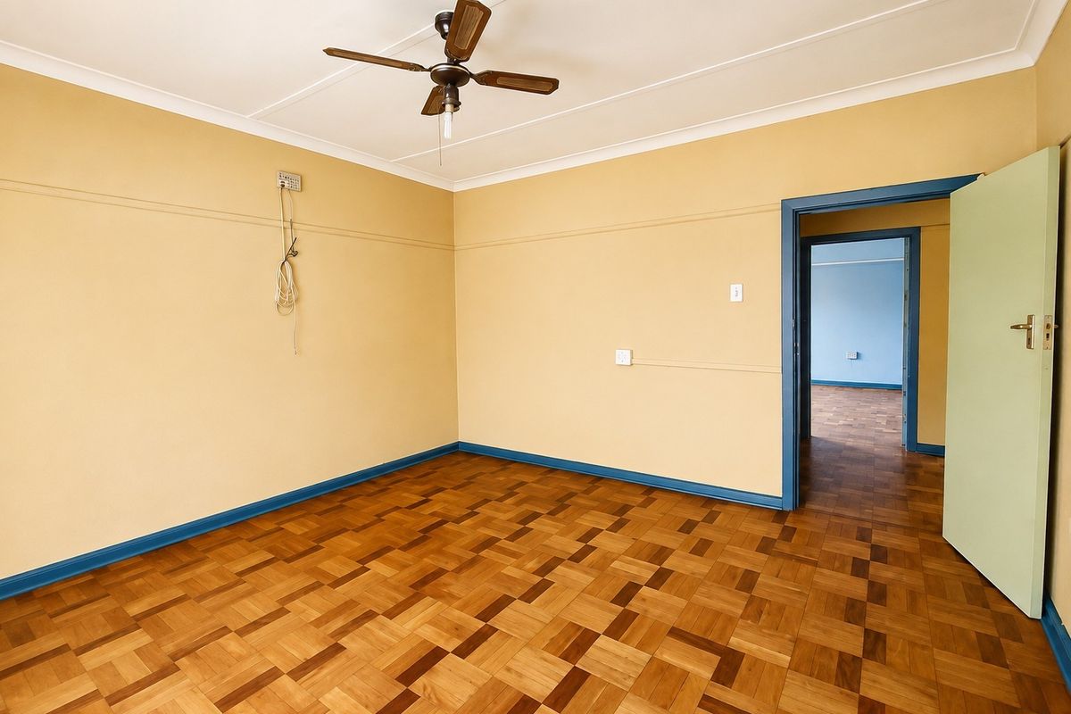 An empty bedroom featuring parquet flooring, a ceiling fan, and coved ceilings, with a view into an adjacent room.