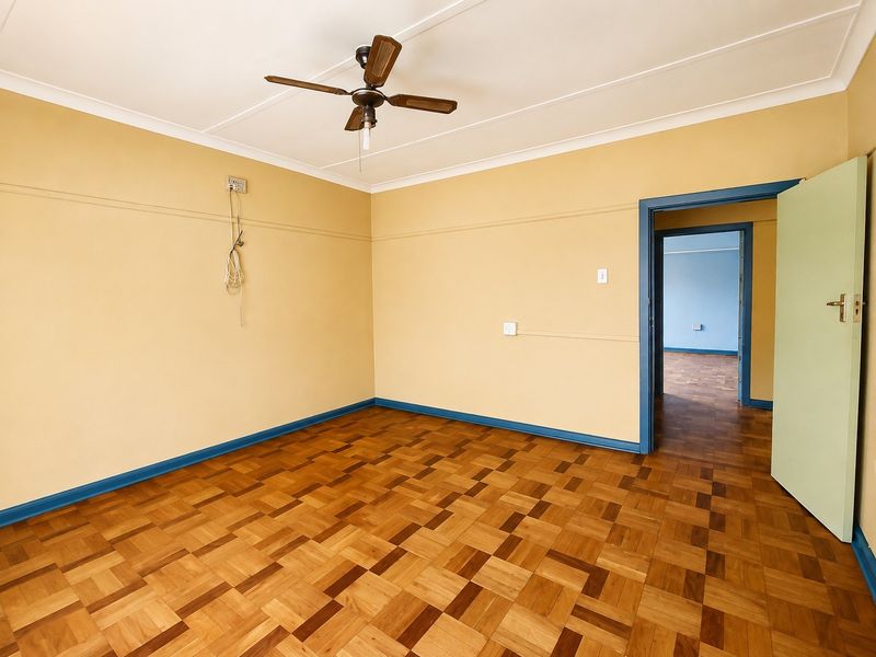 An empty bedroom featuring parquet flooring, a ceiling fan, and coved ceilings, with a view into an adjacent room.