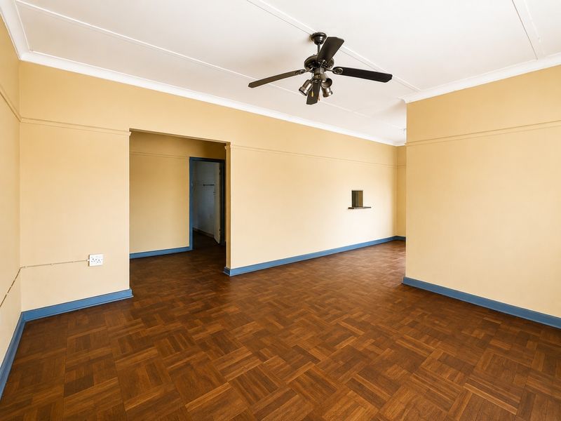 Spacious, empty living area featuring classic parquet flooring, coved cornicing, and a ceiling fan, offering a versatile blank canvas for interior design.