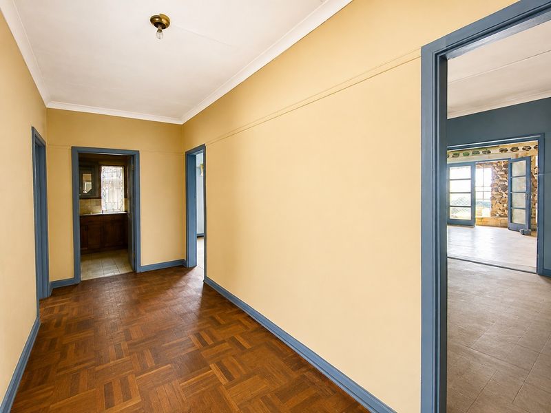 A spacious, empty hallway featuring classic parquet flooring and contrasting blue door frames, providing access to multiple rooms within the home.