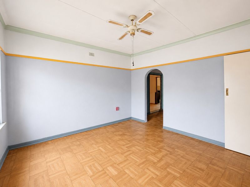 An empty bedroom featuring parquet flooring, a ceiling fan, and a classic arched doorway leading to an adjacent space.