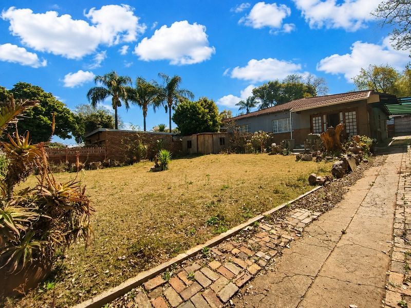 A view of the rear garden featuring a brick-paved walkway, lawn area, and the rear elevation of the house with a tiled roof.