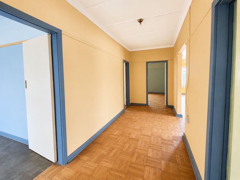 A spacious, empty hallway featuring classic parquet flooring, painted walls with contrasting blue door frames, and access to multiple adjoining rooms.