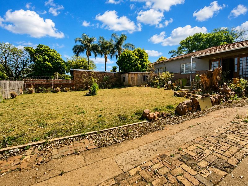 Spacious rear garden featuring a brick-paved driveway, stone retaining wall, and a secure brick boundary wall with razor wire.