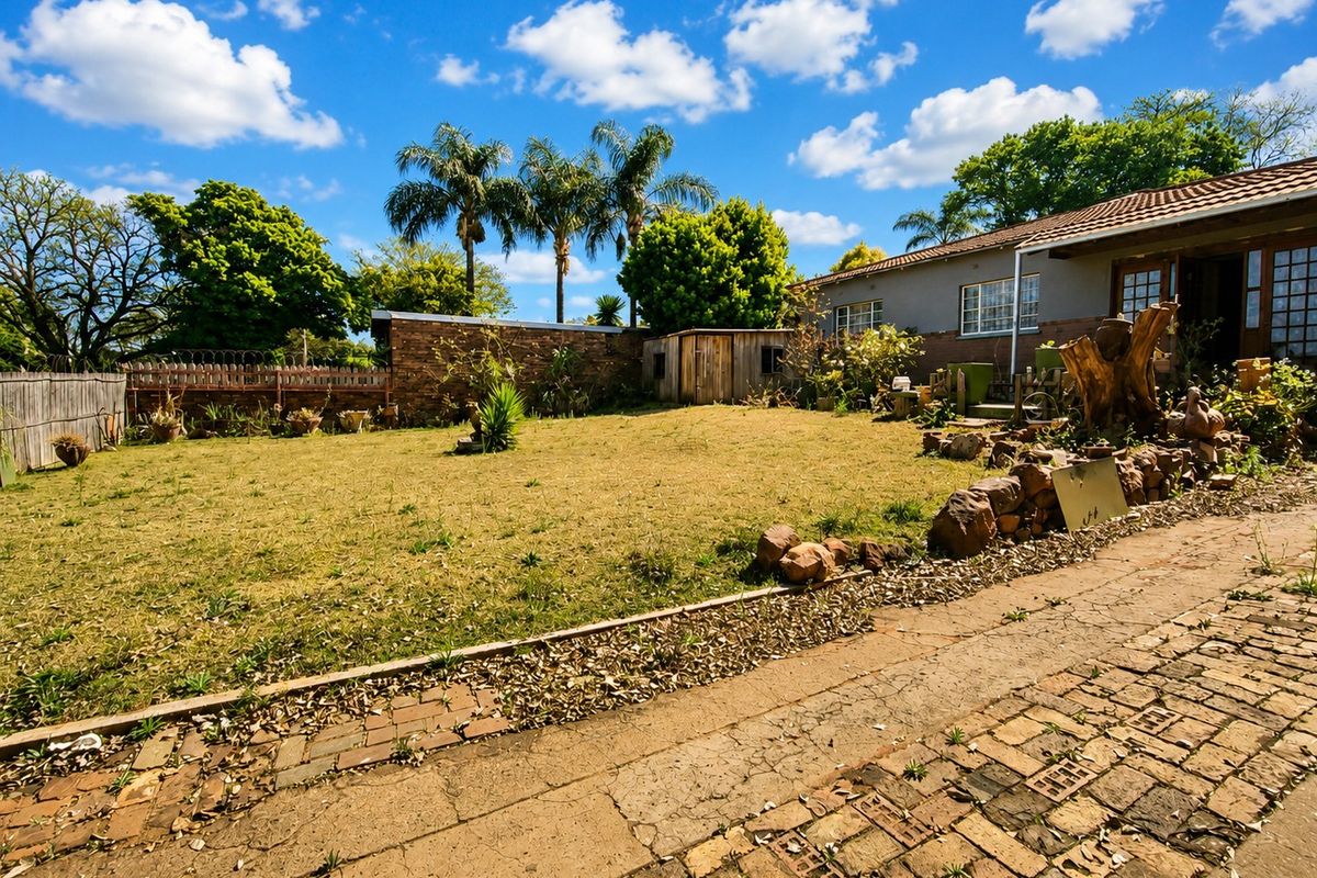 Spacious rear garden featuring a brick-paved driveway, stone retaining wall, and a secure brick boundary wall with razor wire.