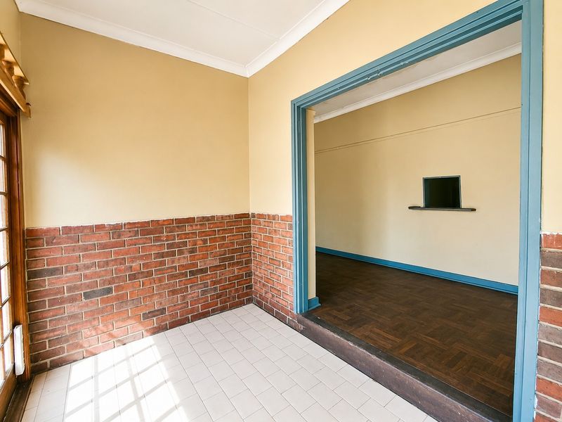 An empty living area featuring a combination of parquet and ceramic tile flooring, brick wainscoting, and a built-in wall shelf.